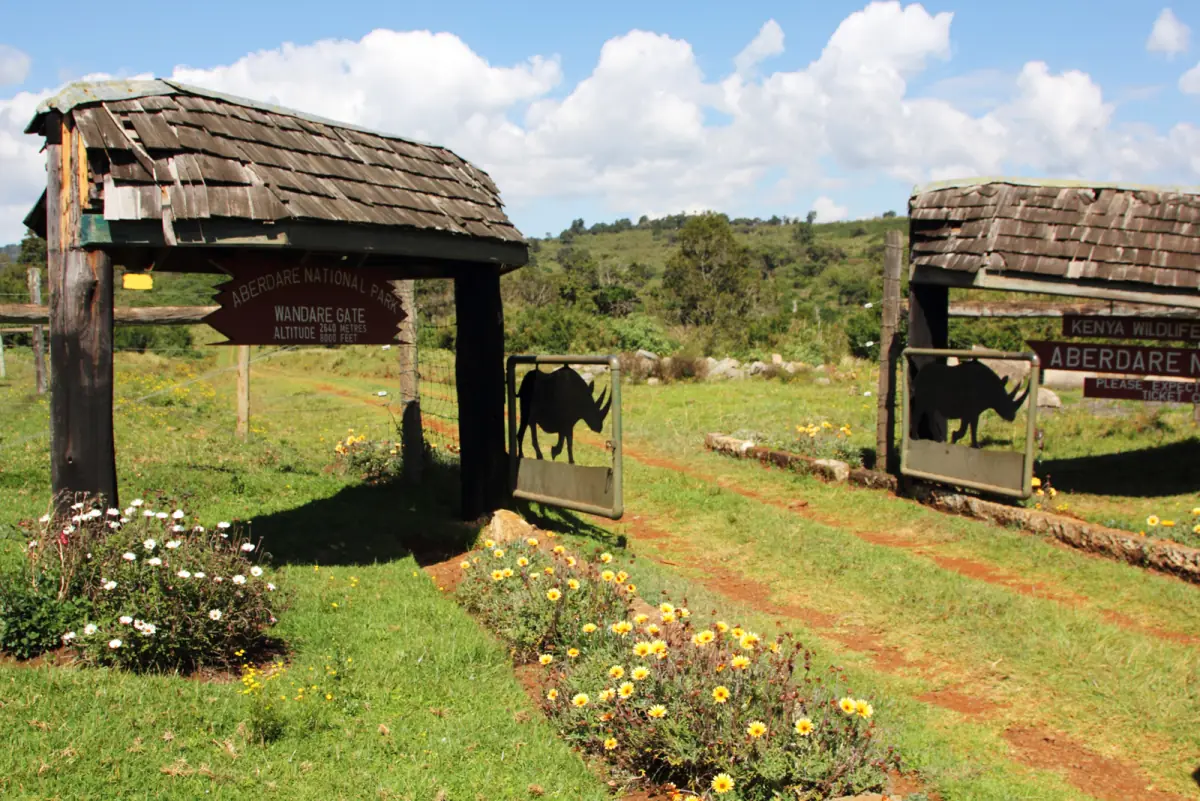 Wooden roofed park entrance gate with flower beds and green hills behind