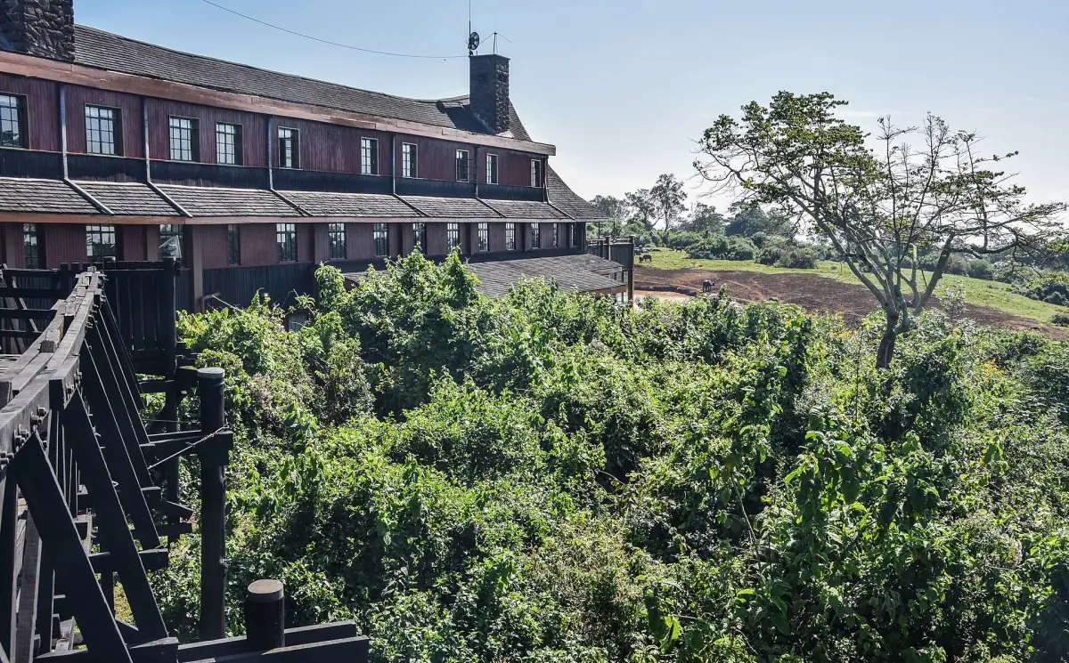Timber lodge with chimneys seen from a wooden balcony over green forest