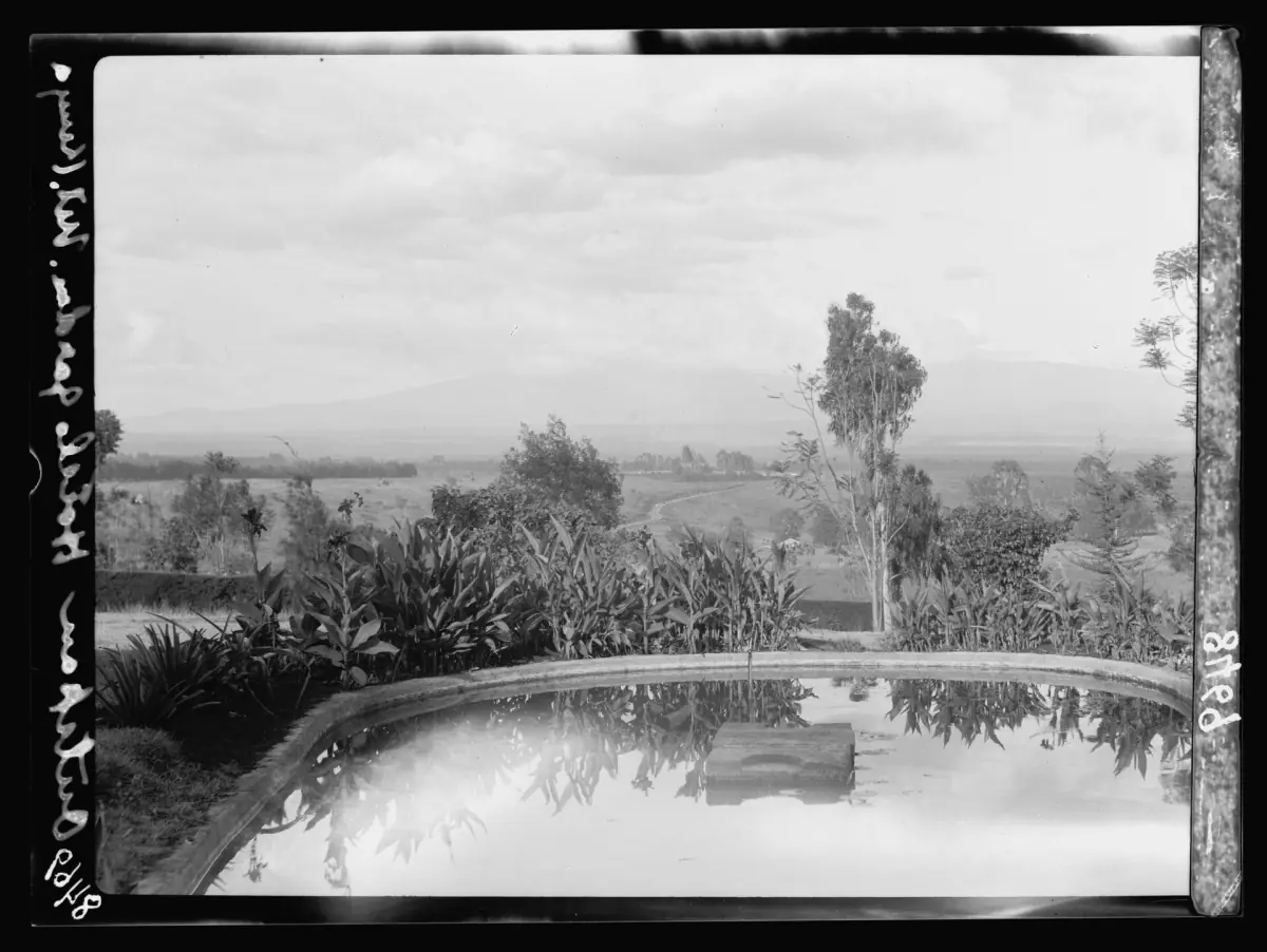 Historische zwart-witfoto met uitzicht over een tuinvijver naar Mount Kenya in de verte